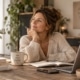 Vrouw zit aan tafel met een kop koffie en een opengeslagen notitieboek en denkt na over hoe ze minder stress kan ervaren